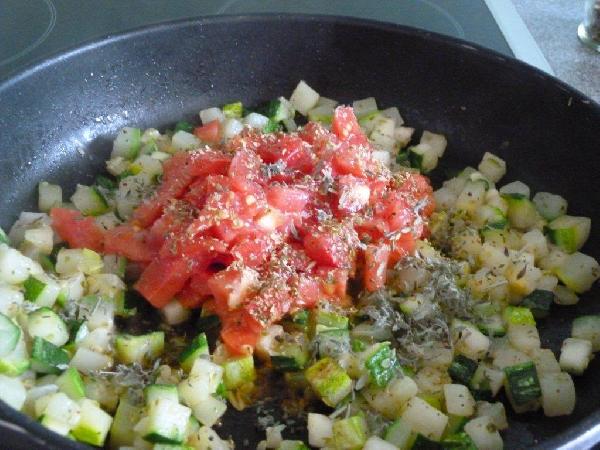 Помидоры также нарезаем маленькими кубиками. В данном случае, я помидоры не очищаю от кожуры. Чеснок чистим и нарезаем мелко-мелко. Выкладываем помидоры к цуккини в сковороду и сразу же выключаем огонь. Добавляем чеснок, орегано, тимьян и черный перец. Лучше будет, если это будет свеже-молотый перец. Можете добавить еще соли, если цуккини недостаточно соленые. Аккуратненько перемешиваем и снимаем с огня. 