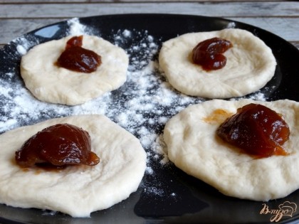 Разделите тесто на небольшие кусочки. Каждый из них разомните руками, чтобы получить небольшую лепешку. Выложите в центр будущего пирожка начинку из густого яблочного повидла.