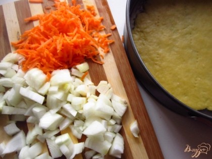 Тесто выложите в форму для выпекания и проткните вилкой. Лук нарежьте, а морковь натрите на терке.