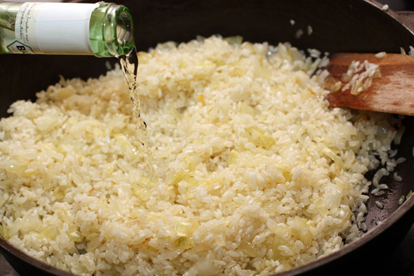 Рис промойте и положите к луку. Готовьте пару минут до прозрачности риса. Затем влейте вино и продолжайте готовить на небольшом огне. 