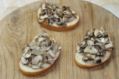 На хлеб выложить готовые запеченные грибы, посыпать мелко рубленным укропом и посыпать твердым сыром.