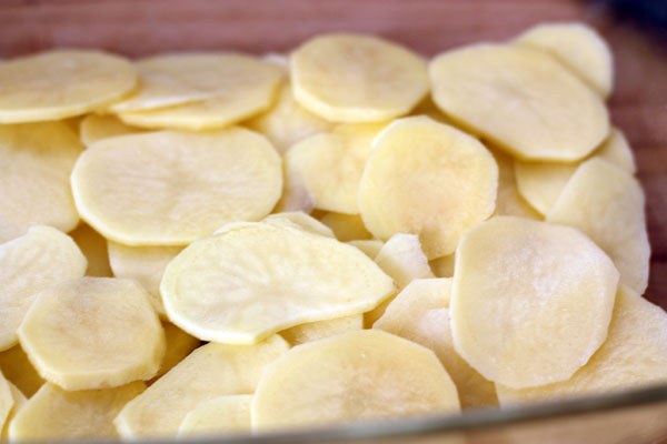 Форму для запекания смажьте маслом и выложите ломтиками картофеля внахлест (должна уйти примерно треть всего объема картошки).