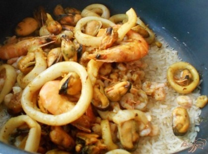 В большой казан или кастрюлю с антипригарным покрытием выложите сырой рис быстрого приготовления. Обжарьте морепродукты, кроме больших креветок, в оставшемся оливковом масле. Добавьте морепродукты к рису.