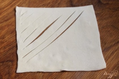 Слоеное тесто раскатываем толщиной 1 мм. И разрезаем на квадраты. В углу квадратов делаем надрезы.