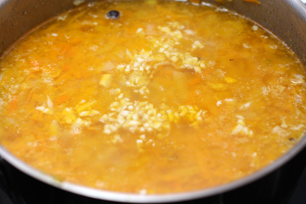 Чеснок нарежьте как можно мельче и положите в суп вместе с сушеной зеленью. Выключите огонь и дайте настояться 5 минут под крышкой.