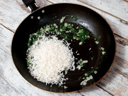 Рис, не промывая, добавить на сковороду. Перемешать и обжарить в масле с зеленью и луком в течение 5-7 минут.