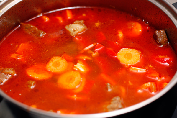 Добавьте в гуляш морковь, перец, помидоры и чеснок, долейте горячей воды и готовьте дальше.