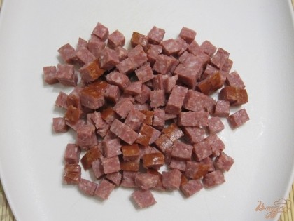 Копченую колбасу нарезать небольшими кубиками.