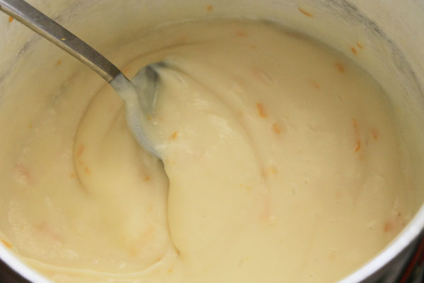 В отдельной миске вскипятите молоко с сахаром, влейте его тонкой струйкой в посуду с желтками, постоянно помешивая. Положите натёртую цедру четверти апельсина. Поставьте посуду на небольшой огонь и, постоянно помешивая, доведите до загустения. Получится густой ванильно-апельсиновый пудинг.