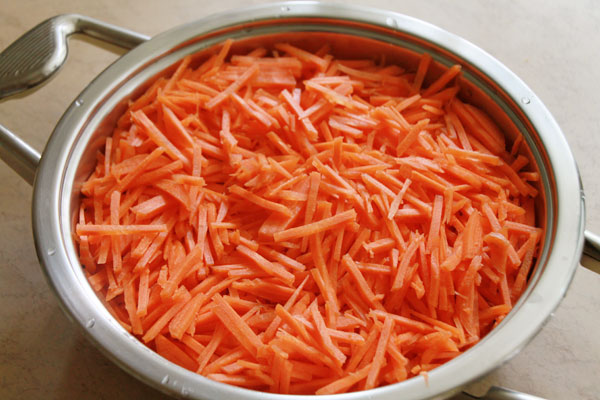 Морковь почистите и натрите на мелкой тёрке. Сложите в холодную кастрюлю, накройте крышкой и поставьте на минимальный огонь.