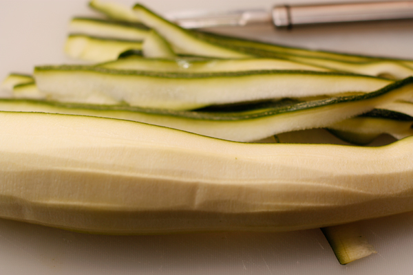 Ножом для чистки овощей срезайте тонкие полоски кабачка так, чтобы на каждой полоске было немного кожицы. Середину с семенами для лапши не используйте.