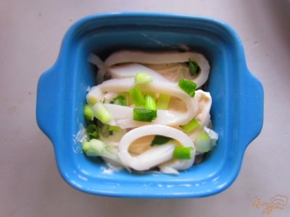 Потом выложите слой кальмаров, посыпьте зеленым луком и смажьте немного сметаной.