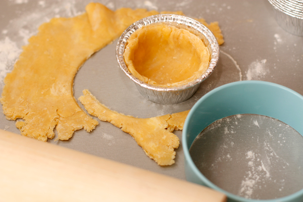 Охлажденное тесто раскатайте тонким слоем (0,3-0,5 см) и вырежьте круги большего диаметра, чем формочки. Выложите тестом формочки и поставьте в морозилку на 15-20 минут.