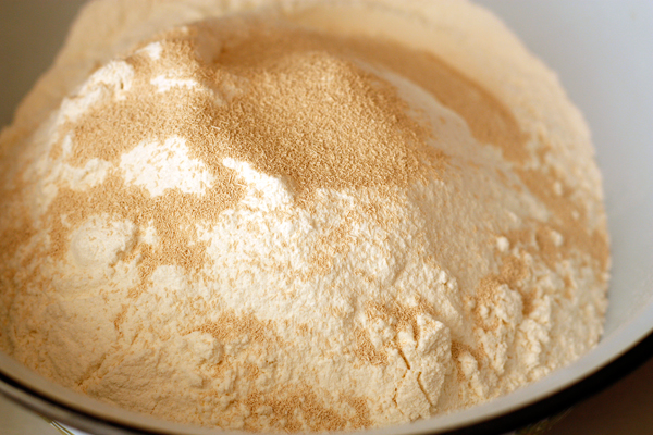 Чтобы приготовить тесто, смешайте просеянную муку с солью и дрожжами. Отдельно соедините 320 мл теплой воды с оливковым маслом. 