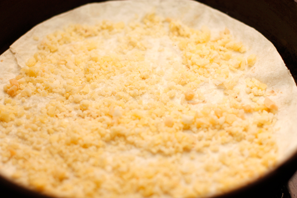На сковороду, немного смазанную маслом, положите тортилью и посыпьте ее измельченным сыром.