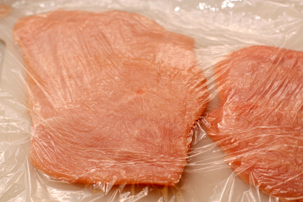 Филе грудки индейки нарежьте пластами толщиной 1-1,5 см, накройте пищевой пленкой и отбейте, чтобы мясо стало тоньше и больше площадью.