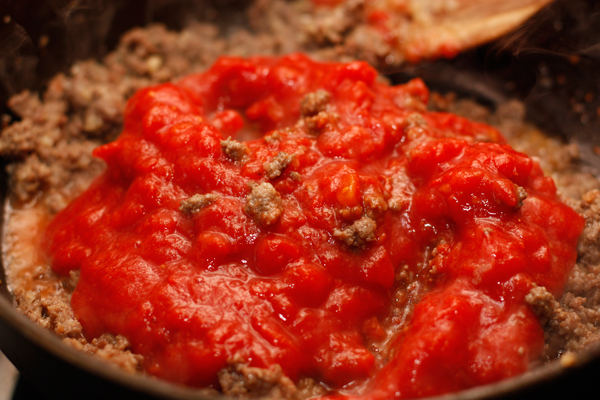 В сковороду к обжаренному фаршу добавить измельченные помидоры без кожицы.