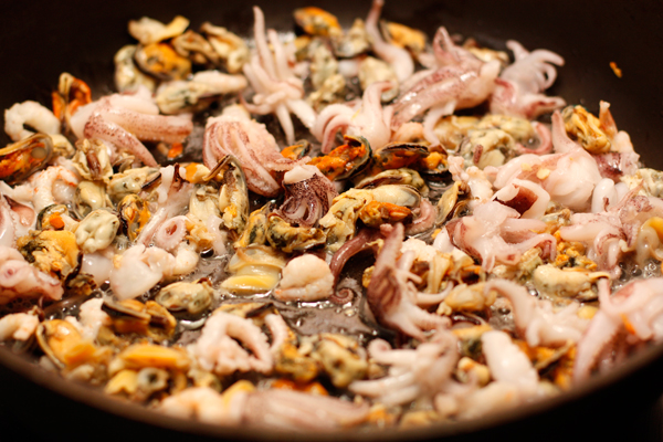 В широкой сковороде нагрейте масло, обжарьте морепродукты в течение 2-3 минут на сильном огне и отложите.