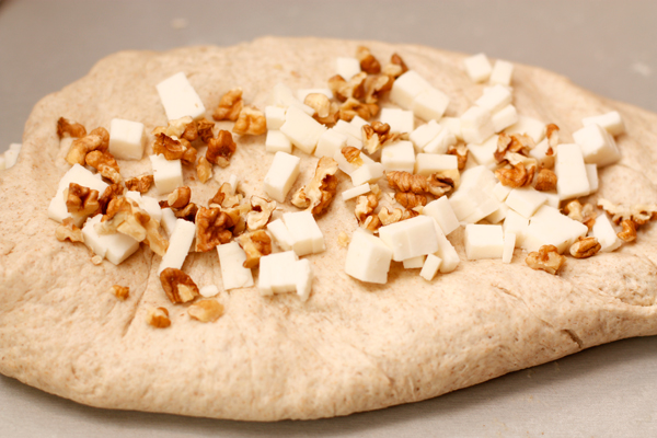 Сделайте из теста лепешку и насыпьте сверху треть сыра и орехов. Закатайте и равномерно распределите начинку в тесте. Повторите этот процесс еще 2 раза.