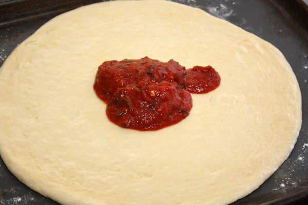 Раскатайте, или лучше, растяните тесто в лепешку толщиной полсантиметра, выложите на посыпанный мукой противень и смажьте оливковым маслом.  Сверху распределите <a href="http://www.foodclub.ru/detail/5685/">соус для пиццы</a>.