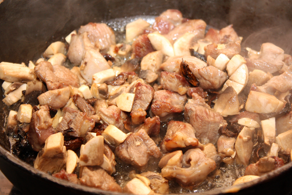 Когда мясо станет светло-коричневым, добавить в сковороду белые грибы вместе с жидкостью и нарезанные шампиньоны. Убавить огонь, влить вино и готовить без крышки 10-15 минут.