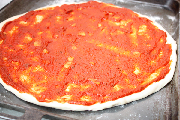 Слегка смажьте тесто оливковым маслом, а затем равномерно распределите по нему томатный соус.