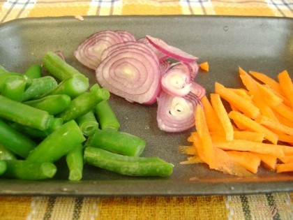 Подготовьте овощи. Морковь следует очистить и нарезать соломкой, фиолетовый лук – кольцами, а замороженную стручковую фасоль просто ополоснуть водой.