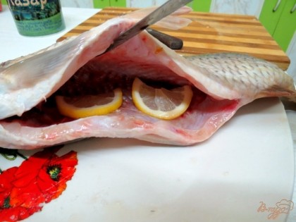 У лимона отрезаем 1 дольку, разрезаем её пополам и вкладываем в брюшко рыбы.С оставшегося лимона выдавливаем сок и им натираем рыбу. Солим и перчим её.