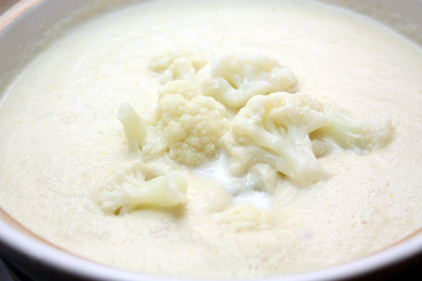 Цветную капусту вместе с жидкостью и лук измельчите в блендере до состояния пюре. Если суп получится слишком густым — добавьте еще молоко или сливки.   Целые соцветия положите в кастрюлю.