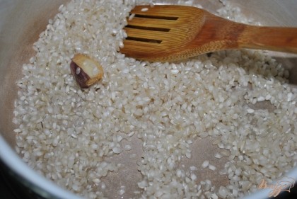 В кастрюлю налить масло и высыпать туда же рис и один зубочек чеснока.Помешивать 2-3 минуты