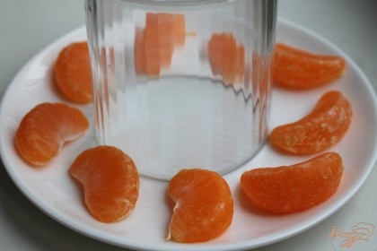 На центр тарелки ставим перевернутый стакан. Чистим мандарин, разделяем его на дольки и раскладываем вокруг стакана.