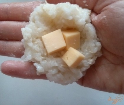 Возьмите в руку немного риса положите сыр и накройте вторым слоем риса, слепите шарик.