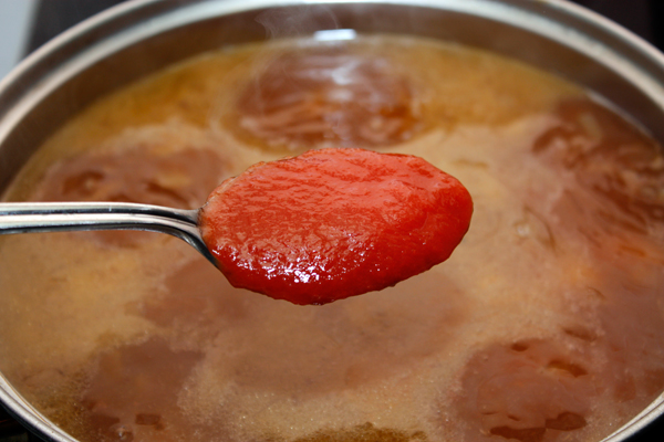 Добавить в суп томатное пюре и мелко нарезанный чеснок.