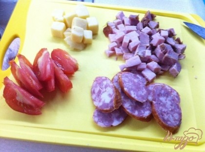 Остальной сыр нарезаем кубиком, мелким кубиком нарезаем ветчину, кружочками полукопченую колбасу и дольками помидор.