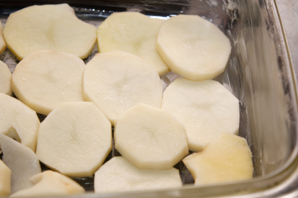 Очищенную и нарезанную тонкими ломтиками картошку выложить одним слоем в форму для запекания, предварительно смазанную маслом.  Картошку полить сливками, посолить, поперчить.
