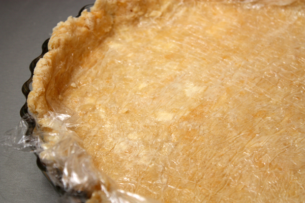 Холодное тесто раскатываем прямо на пищевой пленке с помощью посыпанной мукой скалки до толщины примерно 0,5 см и переворачиваем в форму для пирога.