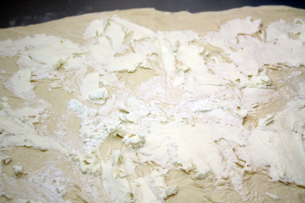 Тесто раскатать на посыпанной мукой поверхности прямоугольником толщиной 0,5 см и намазать творожным сыром.
