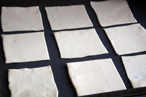 Тесто нужно раскатать толщиной 0,3-0,5 см на слегка посыпанной мукой поверхности и нарезать квадратами примерно 10х10 см.
