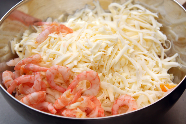 Сыр потереть на крупной терке, добавить к яйцам. Креветки ошпарить кипятком, дать стечь воде и положить в салат.