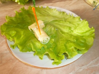 На сервировочную тарелку выкрадываем пару салатных листьев, на них выкладываем сырные рулетики.