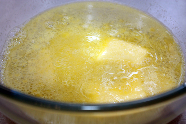 В большую миску положить масло и добавить 300 мл теплой воды, чтобы масло растаяло. Добавить соль и сахар.