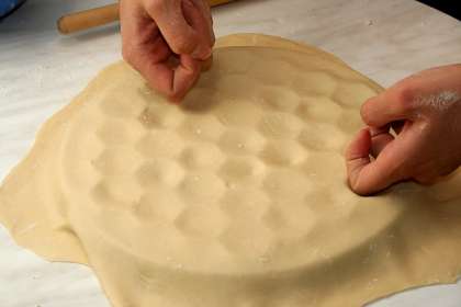 Тесто разделить на 6 равных частей. Таким образом, получится 3 партии пельмешек. Подсыпать муки, чтобы тесто не прилипало и раскатать один кусочек толщиною 2 мм. Накрыть им форму. 