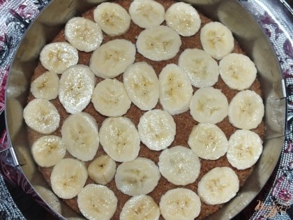 Формируем торт. На основу из печенья выкладываем колечки банана, заливаем половиной творожной массы