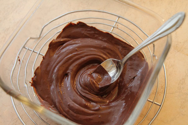 В небольшой мисочке растапливаем на водяной бане плитку любимого горького шоколада. Для этого в широкую кастрюльку нужно налить горячей воды, в воду поместить посудину с поломанным шоколадом и поставить на огонь, чтобы вода постоянно кипела. Таким образом температура вокруг шоколада будет не больше 100 градусов и он не подгорит.<p>Из всей шоколадной массы добавляем к шоколадно-масляному крему (который мы уже сняли с плиты) ровно половину, т.е. 50 грамм, а остальное пойдёт на украшение.<br><br>В самом конце подмешиваем в шоколадный крем две столовые ложки коньяка (для аромата).