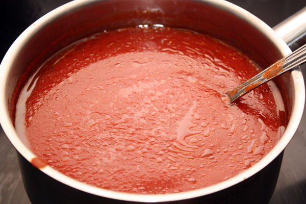 На небольшом огне нагреваем пюре, помешивая время от времени, и добавляем туда оливковое масло, соль и сахар (количество сахара можно менять в зависимости от кислоты томатного пюре). Средняя продолжительность варки соуса — около 20 минут. 