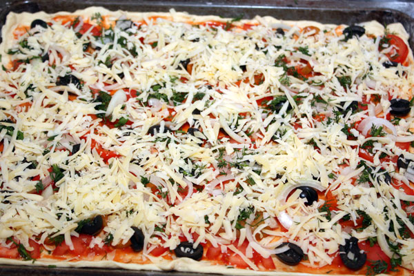 Теперь пиццу нужно обильно посыпать тертым сыром, можно добавить зелени или сушеных трав.