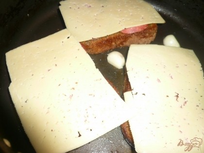 Колбасу прикрываю кусочками сыра. Теперь уже жарю на слабом огне, под крышкой. Надо чтобы хлеб поджарился снизу и расплавился сыр.