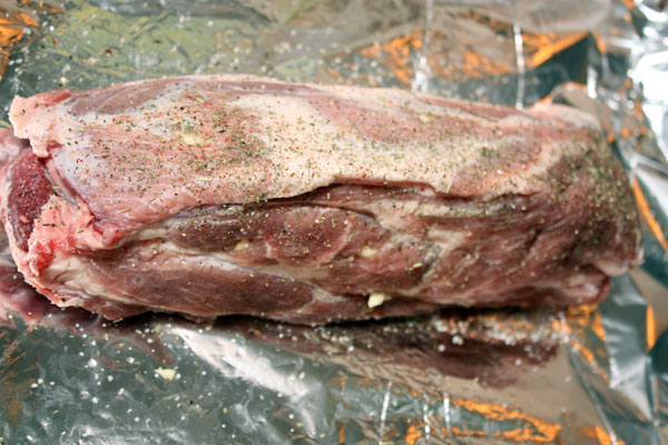 Острым ножом делаем глубокие надрезы в мясе через каждые 5-10 см. В получившиеся отверстия вставляем кусочки чеснока.  Мясо со всех сторон посыпаем солью, перцем и какими-нибудь ароматными травами (по вкусу).