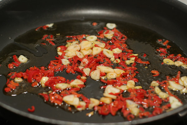 В большой сковороде или воке нагреть масло и обжарить на нем чили и чеснок 1−2 минуты, пока чеснок не станет золотистым.