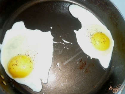 А на сковороду выливаем вторую из указанных в ингредиентах столовую ложку растительного масла, прогреваем и разбиваем яйца. Яйца лучше выложить так, чтобы они не соединялись друг с другом, впрочем это не так важно, всегда можно разрезать потом одну яичницу на две части. Посыпаем яйца солью и черным молотым перцем. Жарим под крышкой до готовности. Если уверены в качестве яиц - оставьте желток жидким.
